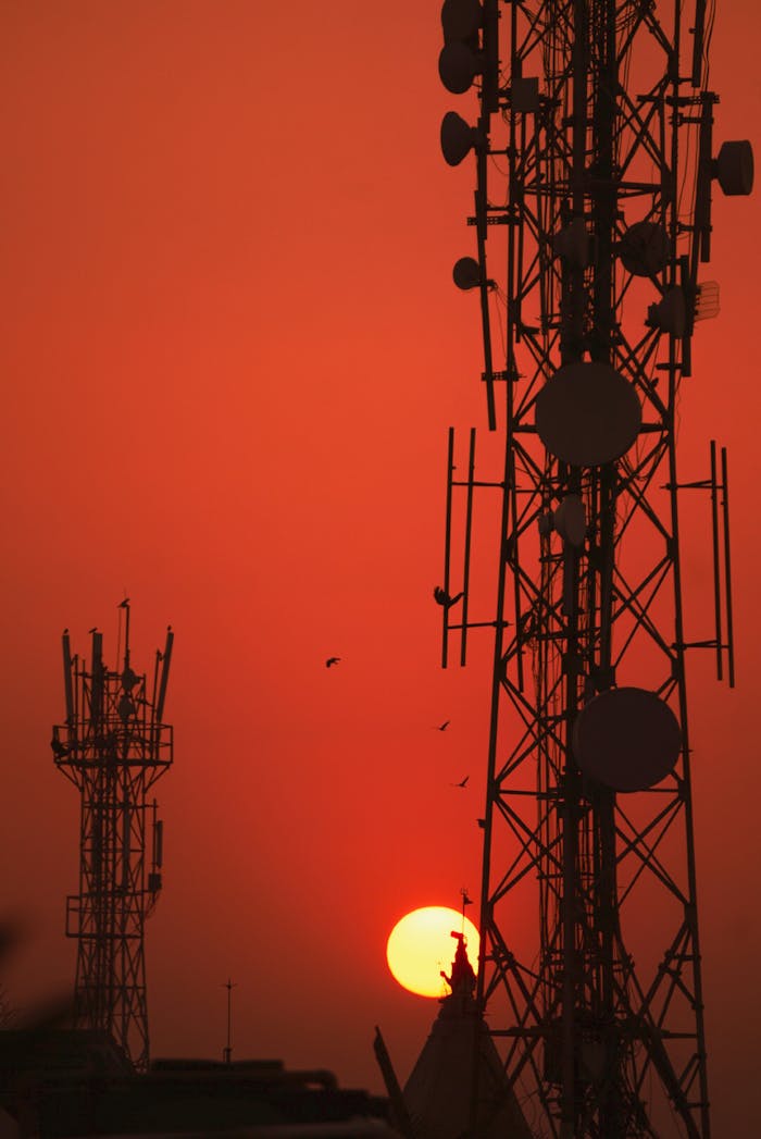 Silhouetted communication towers against a vibrant sunset in India, creating a striking contrast and a serene atmosphere.